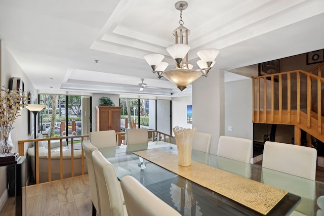 dining area with a notable chandelier, wood-type flooring, and a raised ceiling