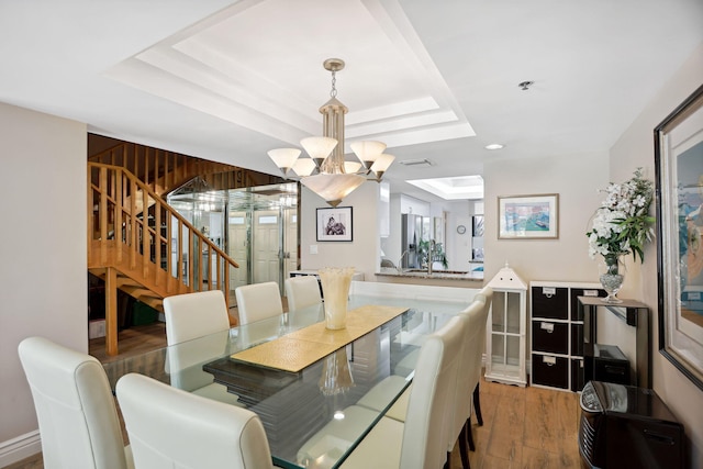 dining area featuring a raised ceiling, hardwood / wood-style flooring, and an inviting chandelier