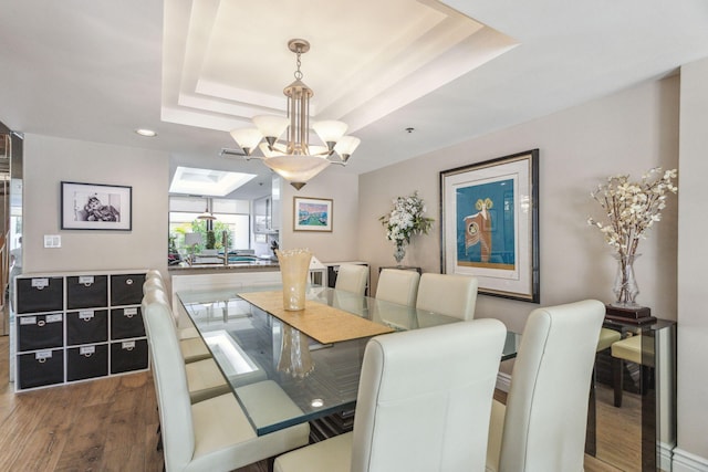 dining room with a notable chandelier, dark wood-type flooring, and a raised ceiling