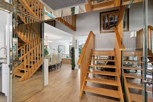 staircase with a chandelier, a towering ceiling, and light wood-type flooring