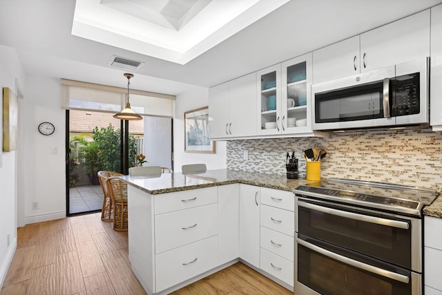 kitchen with appliances with stainless steel finishes, dark stone counters, tasteful backsplash, light hardwood / wood-style flooring, and white cabinets