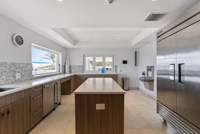 kitchen featuring light tile floors, a kitchen island, backsplash, and a raised ceiling