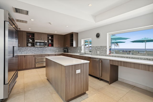 kitchen featuring light tile floors, stainless steel appliances, a center island, backsplash, and sink