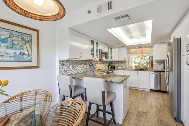 kitchen featuring appliances with stainless steel finishes, tasteful backsplash, dark stone countertops, kitchen peninsula, and a chandelier