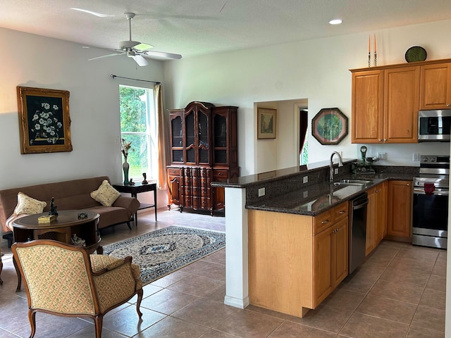 kitchen with stainless steel appliances, sink, tile patterned floors, dark stone counters, and ceiling fan