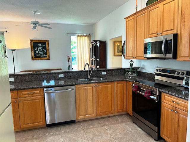 kitchen featuring appliances with stainless steel finishes, sink, light tile patterned floors, ceiling fan, and dark stone countertops