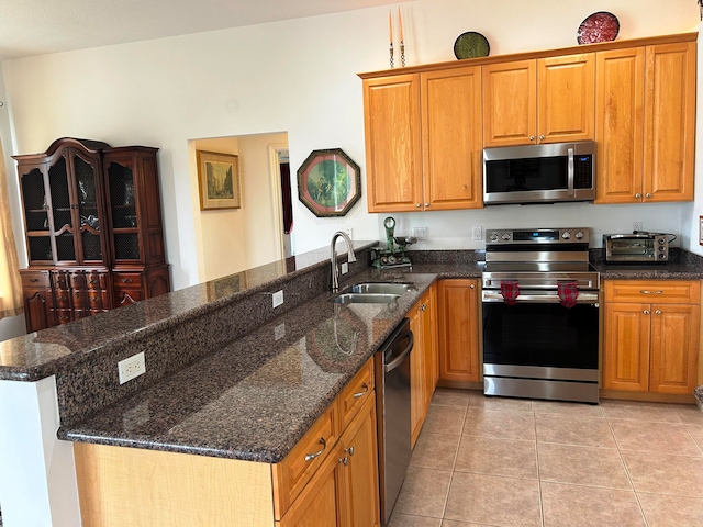 kitchen featuring appliances with stainless steel finishes, light tile patterned floors, sink, and dark stone counters