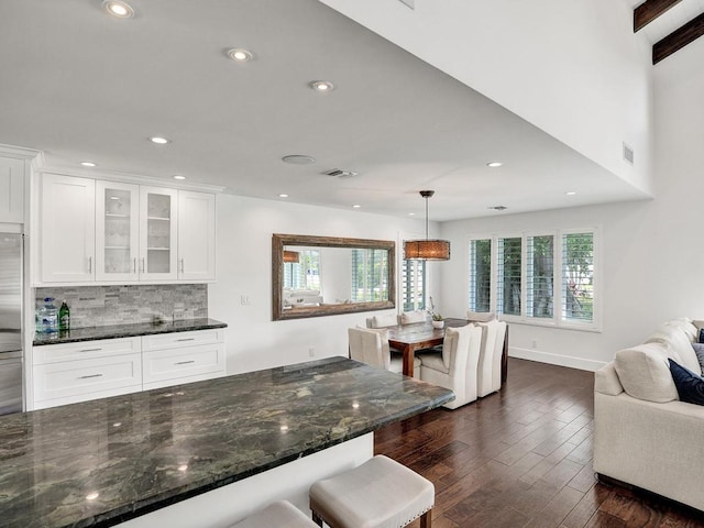 kitchen featuring dark wood-type flooring, white cabinets, dark stone counters, tasteful backsplash, and pendant lighting