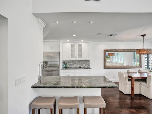 kitchen with decorative light fixtures, high end fridge, backsplash, white cabinetry, and a kitchen breakfast bar