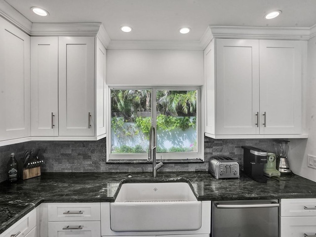 kitchen with stainless steel dishwasher, white cabinetry, backsplash, dark stone countertops, and sink