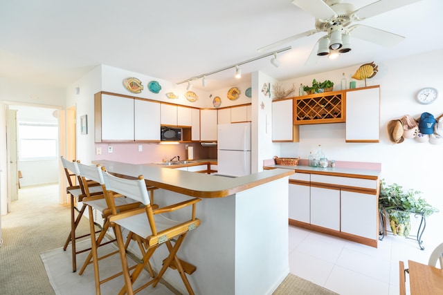 kitchen with light colored carpet, track lighting, white cabinetry, white refrigerator, and a breakfast bar