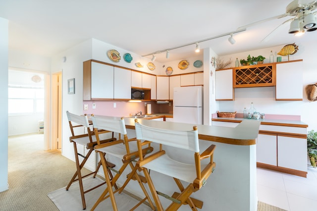 kitchen featuring white fridge, a kitchen bar, light carpet, white cabinetry, and rail lighting