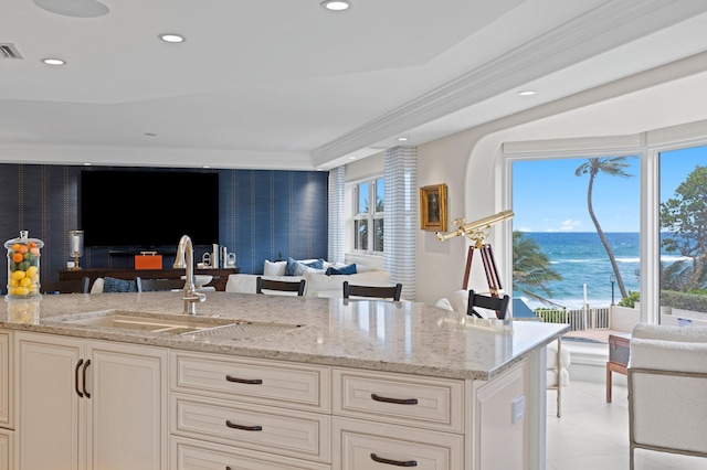 kitchen featuring a water view, light tile floors, white cabinets, sink, and light stone countertops