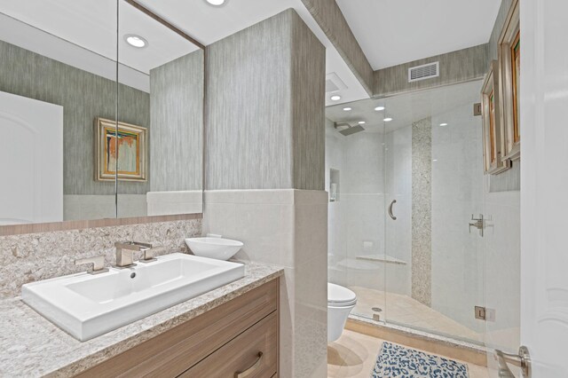 bathroom with tile floors, vanity, tile walls, a shower with shower door, and toilet