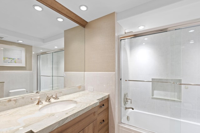 full bathroom with tile walls, toilet, bath / shower combo with glass door, and vanity