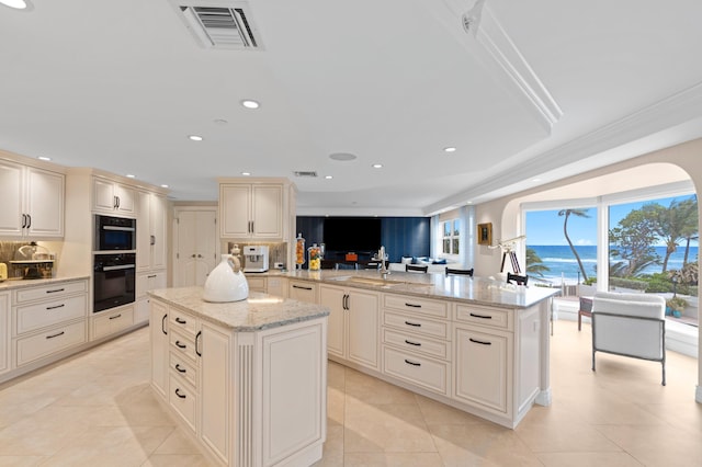 kitchen featuring a kitchen island, a water view, light stone counters, black double oven, and light tile floors