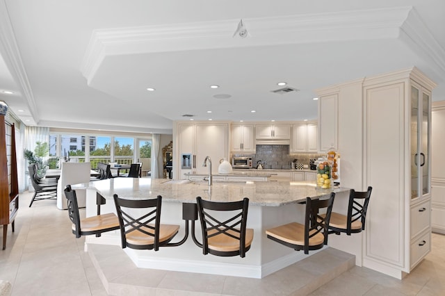 kitchen featuring backsplash, a breakfast bar area, light tile flooring, cream cabinetry, and light stone counters