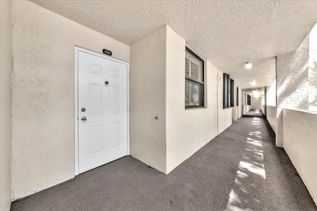 corridor featuring a textured ceiling and dark colored carpet