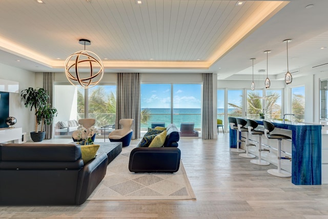 living room with a tray ceiling, light wood-type flooring, and a water view