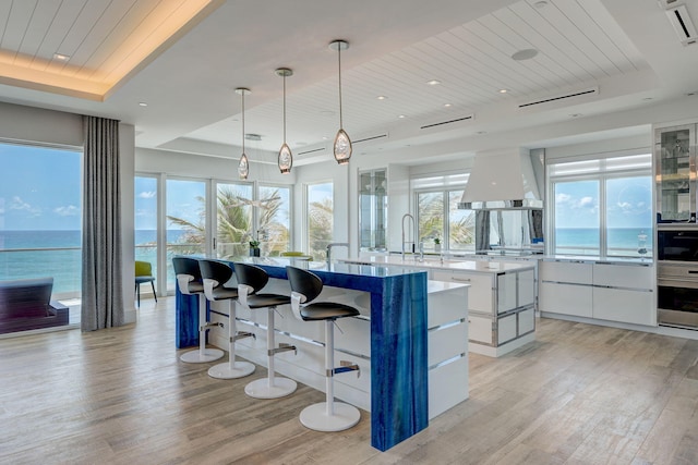 kitchen with light hardwood / wood-style flooring, an island with sink, decorative light fixtures, oven, and wall chimney exhaust hood