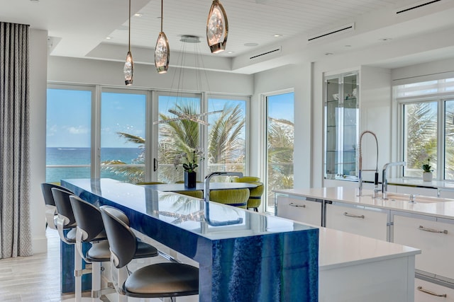 kitchen featuring a healthy amount of sunlight, white cabinets, a water view, and hanging light fixtures