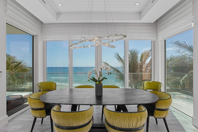 dining area with light hardwood / wood-style floors, a water view, and a raised ceiling