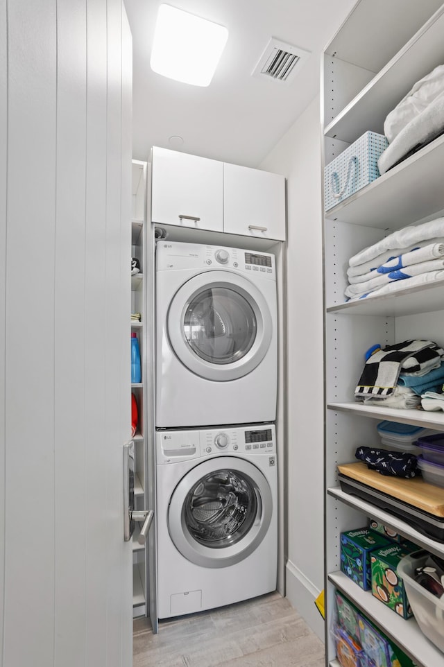 washroom with stacked washing maching and dryer and light wood-type flooring