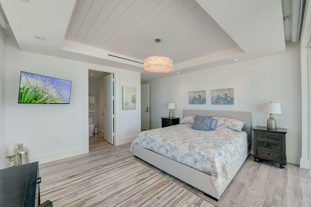 bedroom with ensuite bath, a tray ceiling, and light wood-type flooring