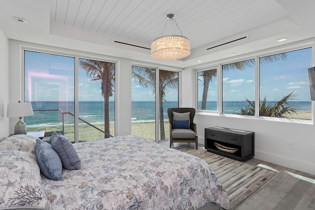 bedroom with a tray ceiling, access to outside, hardwood / wood-style flooring, and a water view