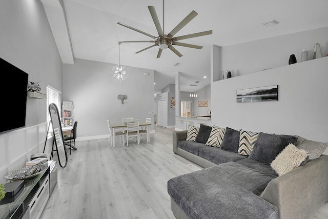 living room with high vaulted ceiling, light hardwood / wood-style flooring, and ceiling fan with notable chandelier