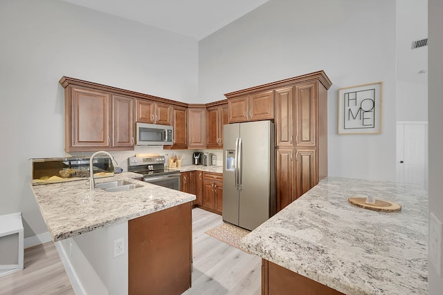 kitchen featuring light stone countertops, light hardwood / wood-style floors, kitchen peninsula, a high ceiling, and appliances with stainless steel finishes