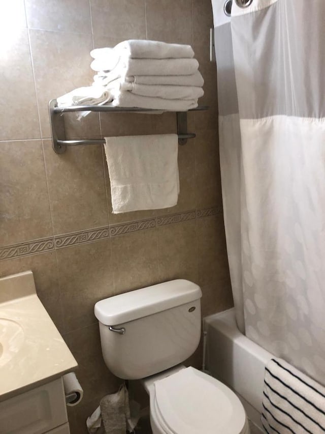 full bathroom with tile walls, toilet, vanity, and shower / bathtub combination with curtain