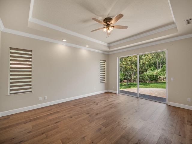 empty room with a raised ceiling, crown molding, and wood-type flooring