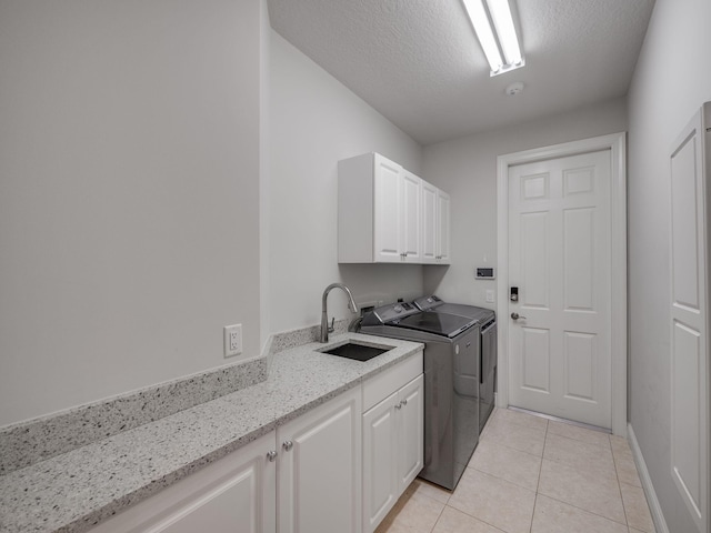 laundry room with a textured ceiling, washing machine and dryer, light tile patterned floors, sink, and cabinets