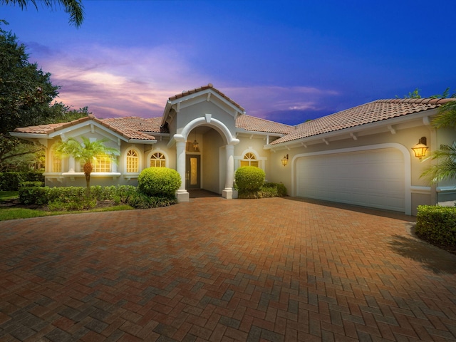 mediterranean / spanish-style house with decorative driveway, stucco siding, an attached garage, and a tiled roof