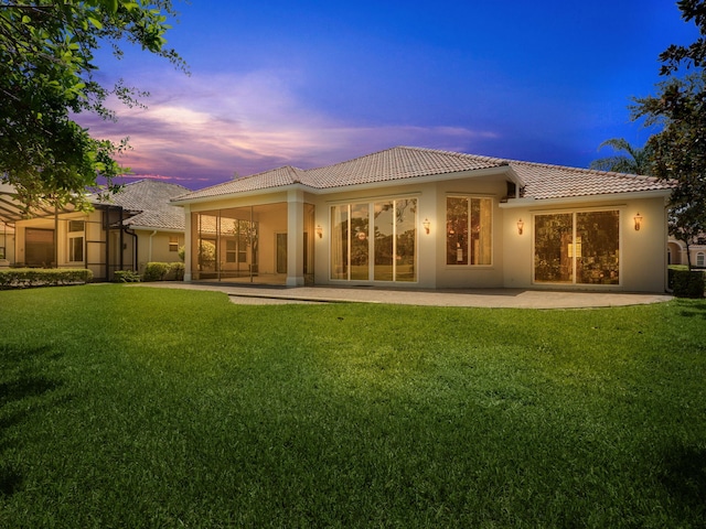 back house at dusk featuring a patio area and a yard