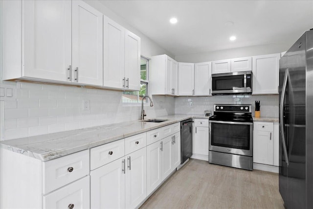 kitchen featuring light wood finished floors, appliances with stainless steel finishes, white cabinetry, a sink, and light stone counters
