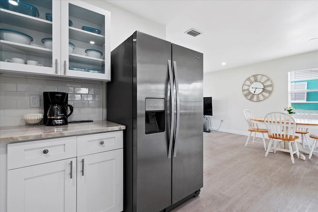 kitchen featuring visible vents, tasteful backsplash, glass insert cabinets, stainless steel refrigerator with ice dispenser, and light wood-type flooring