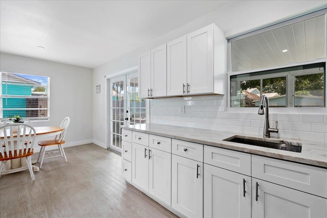 kitchen featuring backsplash, a sink, light stone countertops, and a wealth of natural light