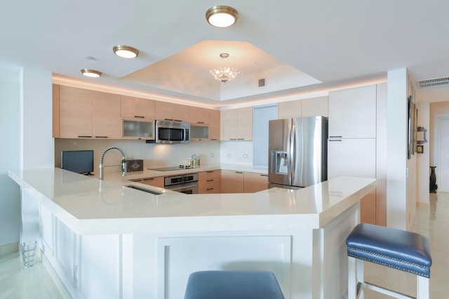 kitchen featuring appliances with stainless steel finishes, a breakfast bar, sink, kitchen peninsula, and a raised ceiling