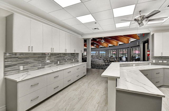 kitchen with light stone countertops, ceiling fan, beam ceiling, backsplash, and white cabinetry