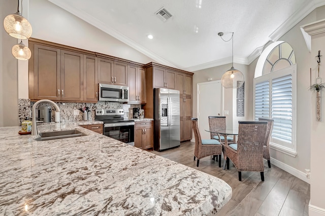 kitchen with tasteful backsplash, vaulted ceiling, hanging light fixtures, sink, and appliances with stainless steel finishes