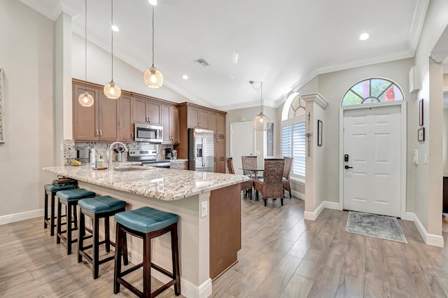 kitchen with stainless steel appliances, light stone counters, light hardwood / wood-style flooring, and decorative light fixtures