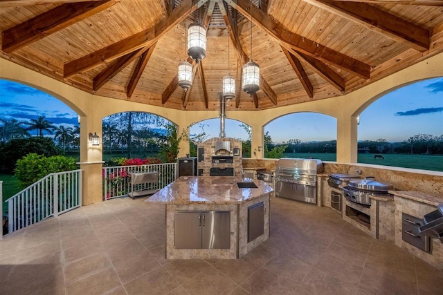 patio terrace at dusk with a gazebo, a grill, and exterior kitchen