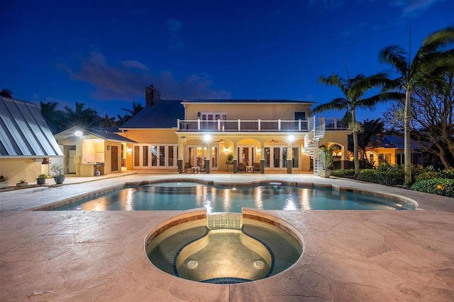 pool at night with a patio area and an in ground hot tub