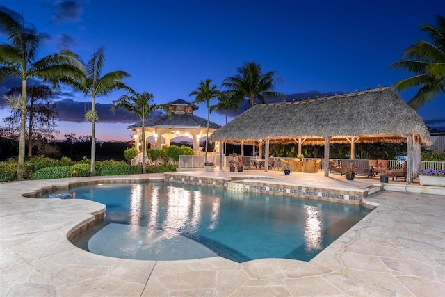 pool at dusk with a gazebo and a patio area