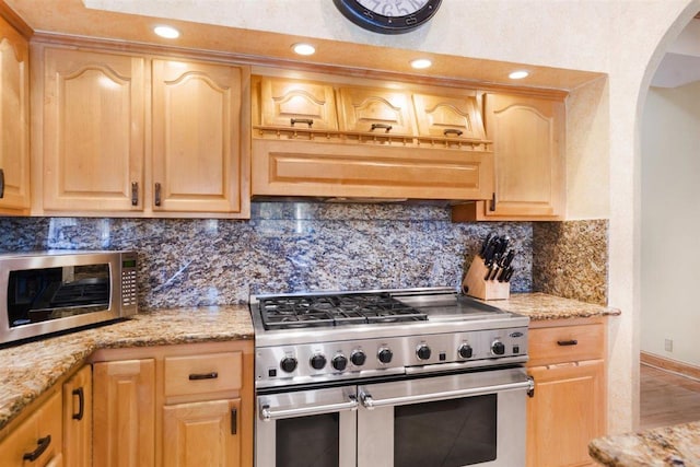 kitchen with backsplash, light brown cabinets, stainless steel appliances, and light stone countertops