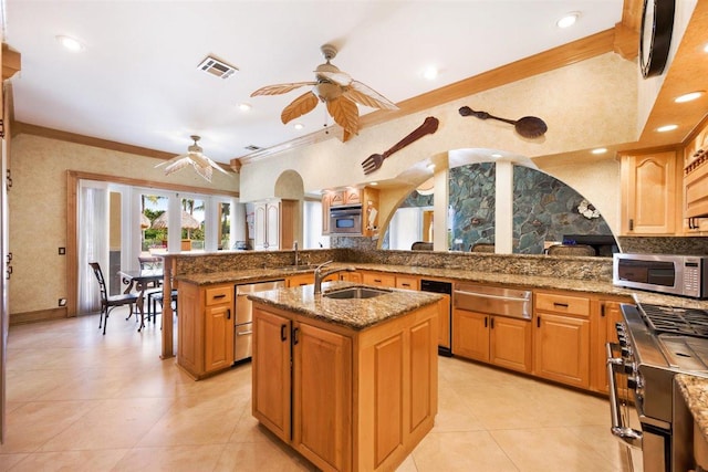 kitchen featuring dark stone counters, stainless steel appliances, ceiling fan, and an island with sink