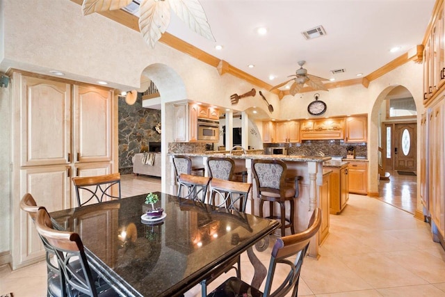 tiled dining area featuring ornamental molding, sink, ceiling fan, and a stone fireplace