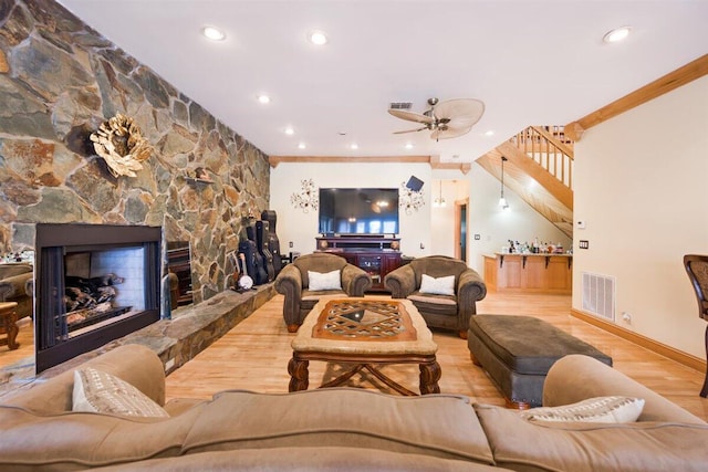 living room with crown molding, a fireplace, ceiling fan, and light wood-type flooring